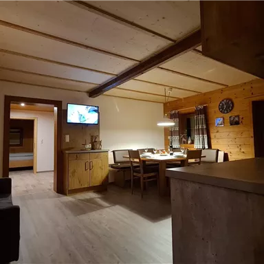 A cozy apartment with wood paneling and modern furniture. The room is brightly lit and has a dining table as well as a small kitchen.