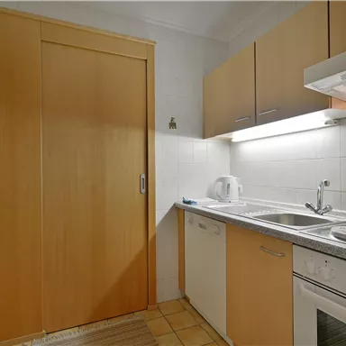 Eine moderne Küche mit hellen Holzschränken und einer hellen Arbeitsfläche. Die Ausstattung umfasst einen Herd, Backofen und Spüle.