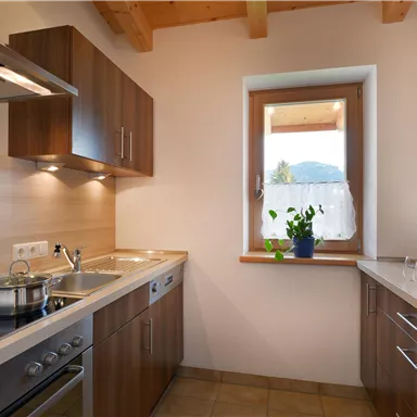 Eine moderne Küche mit Holzschränken und hellen Wänden. Es gibt einen Fenster mit Blick ins Freie und eine Kochfläche.