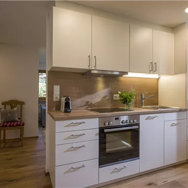 Eine moderne Küche mit weißen Schränken und Holzfußboden. Licht kommt durch ein Fenster, das den Raum freundlich und einladend macht.