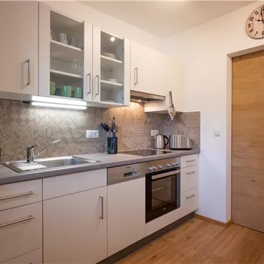 A modern kitchen with bright cabinets and a stainless steel sink. It includes a stove, a refrigerator, and a wooden door.