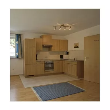 Eine moderne Küche mit hellen Holzschränken und einem Herd. Der Raum ist gut beleuchtet und hat einen Teppich auf dem Boden.