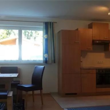 Eine helle, moderne Küche mit Essbereich. Es gibt eine Holztisch und Stühle sowie eine große Fensterfront mit Blick ins Freie.