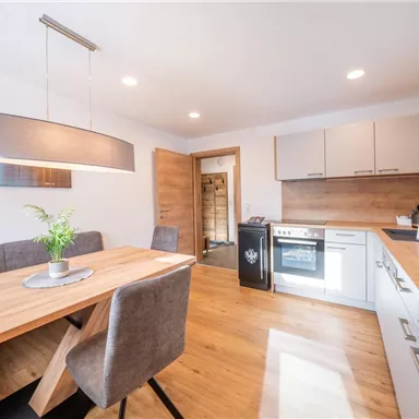 Eine moderne Küche mit einem Essbereich und einem Holztisch. Die Wände sind hell und die Möbel sind stilvoll eingerichtet.