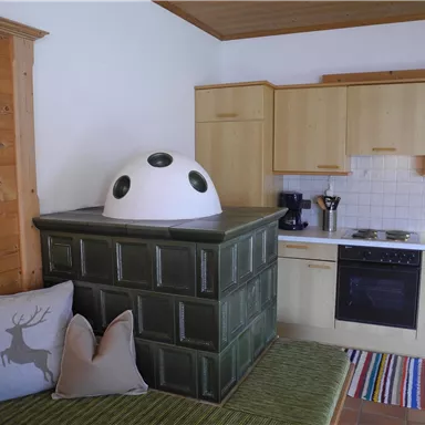 Eine gemütliche Küche mit einer grünen Herdbank und modernen Geräten. Auf dem Boden liegt ein bunter Teppich und es gibt dekorative Kissen auf der Bank.