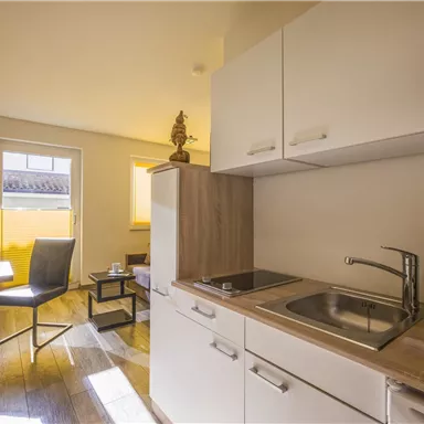 A modern, bright kitchen with a small seating area and large windows. The decor is functional and inviting.