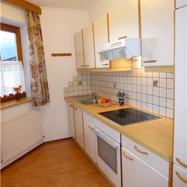 Eine moderne Küche mit weißen Schränken und Holzdetails. Es gibt einen Herd, eine Spüle und Obst auf der Arbeitsplatte.