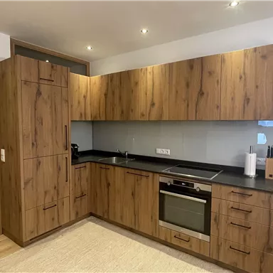 Eine moderne Küche mit Holzschränken und schwarzer Arbeitsplatte. Sie enthält grundlegende Küchengeräte und einen einladenden Essbereich.