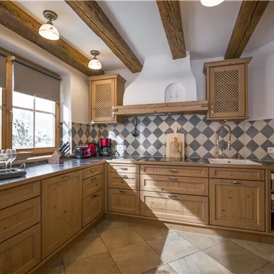 Eine moderne Küche mit Holzmöbeln und einer gefliesten Wand. Große Fenster lassen viel Tageslicht herein.