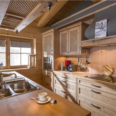Eine gemütliche Holz-Küche mit modernen Geräten und vielen Fenstern, die viel Licht hereinlassen. Auf dem Tisch steht eine Tasse, und es herrscht eine warme Atmosphäre.