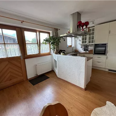 Eine helle und einladende Küche mit Holzfußboden und großen Fenstern. Das Innendesign ist modern und bietet einen offenen Raum mit Pflanzen.