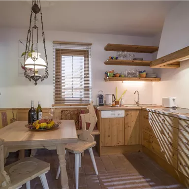 A cozy kitchen with wooden furniture and a round table. Light filters through the window, creating an inviting atmosphere.