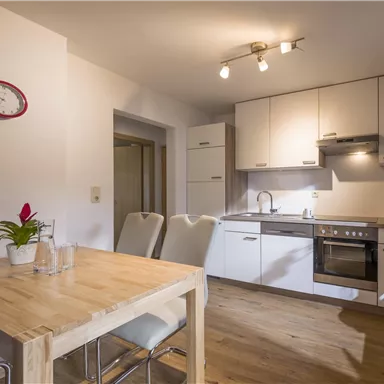 A modern kitchen with light wood and white cabinets. A dining table and chairs complement the space.