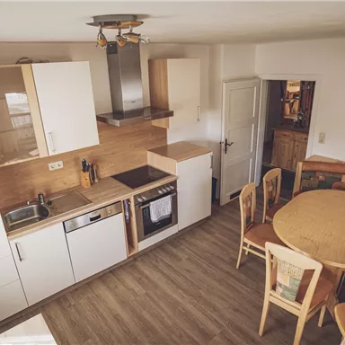A modern kitchen with white cabinets and wooden details. The dining area features a round table and upholstered benches.