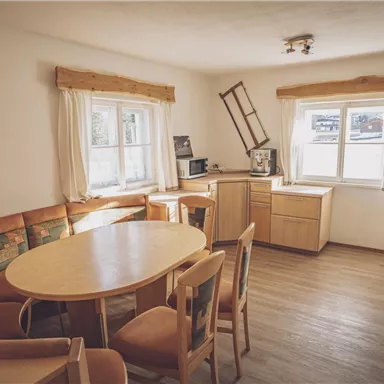 A cozy kitchen with a round table and a corner bench. Large windows provide plenty of light and an inviting atmosphere.