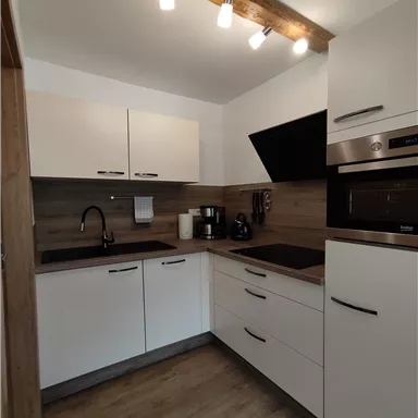 Eine moderne Küche mit weißen Schränken und Holzdetails. Die Ausstattung umfasst eine Spüle, einen Herd und verschiedene Küchengeräte.