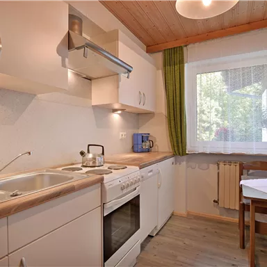 Eine moderne Küche mit weißen Schränken und Holzoberflächen. Ein Esstisch mit Stühlen und Fenster mit Blick ins Freie.