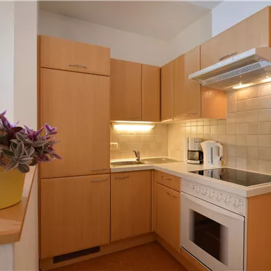 A modern kitchen with wooden cabinets and bright walls. It is equipped with a stove, an oven, and a coffee machine.