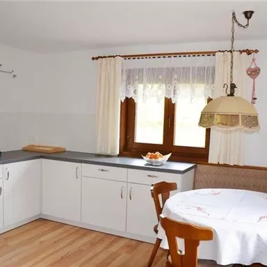 Eine helle Küche mit modernen Möbeln und einem gemütlichen Essbereich. Der Tisch ist mit einer weißen Tischdecke gedeckt und es gibt frisches Obst in einer Schüssel.