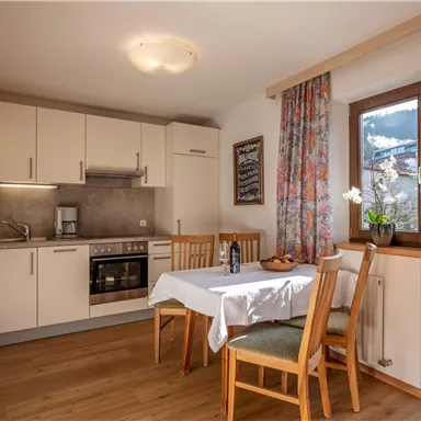 Eine helle Küche mit einem Esstisch und Stühlen. Großzügige Fenster bieten einen Blick auf die Umgebung.