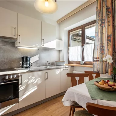 Eine moderne Küche mit weißen Schränken und Edelstahlgeräten. Ein Tisch mit Obstschale und frischen Blumen sorgt für eine einladende Atmosphäre.