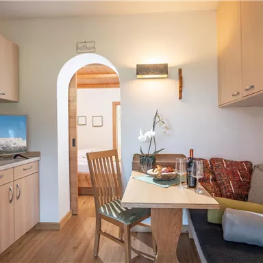 Ein gemütlicher Wohnraum mit einem Tisch, Stühlen und einem Fernseher. Der Raum hat helle Holzmöbel und einen einladenden Look.