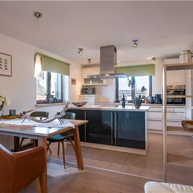 Eine moderne Küche mit einem offenen Wohnbereich. Große Fenster lassen viel Licht herein und es gibt stilvolle Möbel und Dekoration.