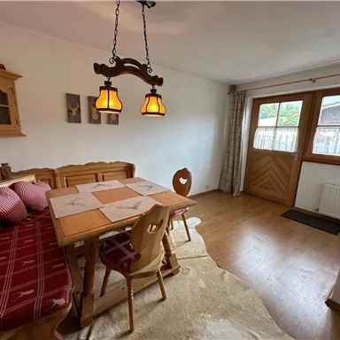 Ein gemütlicher Essbereich mit einem Holztisch und einer Bank. Die Fenster lassen viel Tageslicht hereinfällt und schaffen eine einladende Atmosphäre.