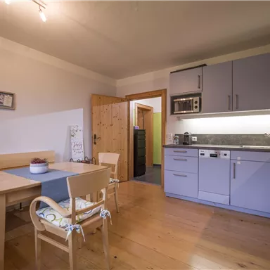 A modern kitchen with blue cabinets and a light wood surface. There is a small dining area with a table and chairs.