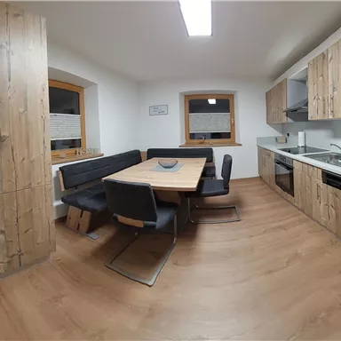 A modern kitchen with wooden cabinets and a large dining table. The space is bright and invitingly designed.