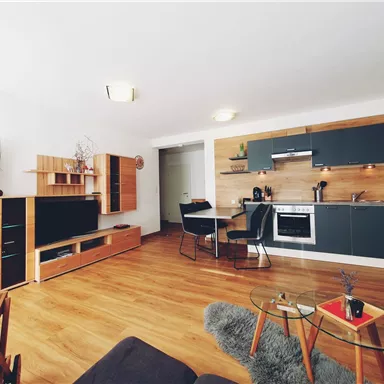 Eine moderne Wohnung mit einer offenen Küche und einem stilvollen Wohnbereich. Der Boden ist aus Holz, und es gibt gemütliche Möbel sowie eine kleine Tischfläche.