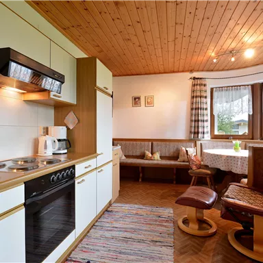 Eine gemütliche Küche mit Holzdecke und modernen Geräten. Auf der rechten Seite befindet sich eine Sitzecke mit Fenster und einem Teppich.