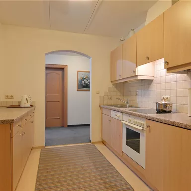 Eine moderne Küche mit Holzschränken und einer Arbeitsplatte aus Stein. Der Raum ist hell und bietet einen guten Überblick über die angrenzenden Bereiche.