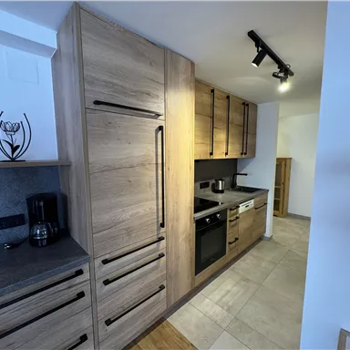 Eine moderne Küche mit Holzschränken und grauen Arbeitsflächen. Die Ausstattung umfasst einen Kühlschrank, einen Herd und eine Spüle.