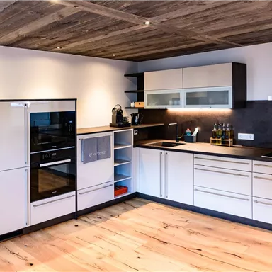 A modern kitchen with hardwood floors and elegant, minimalist furniture. The amenities include a refrigerator, an oven, and a sink.