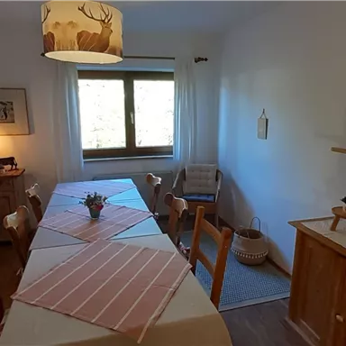 Ein einladender Essbereich mit einem langen Tisch und Stühlen. Das Zimmer ist hell und freundlich mit einem Fenster, das auf die Außenseite blickt.