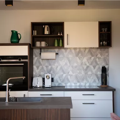 A modern kitchen with wooden and white cabinets. The wall is decorated with gray patterned tiles.