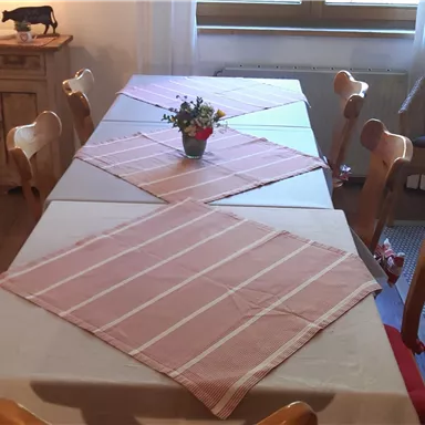 Ein stilvoller Essbereich mit einem langen Tisch und Holzstühlen. Auf dem Tisch liegt ein helles Tischdecken und eine kleine Blumenpflanze als Dekoration.