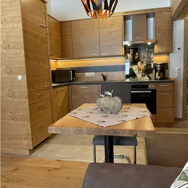 Eine moderne Küche aus Holz mit einem Esstisch und eleganter Beleuchtung. Die Ausstattung ist funktional und gemütlich.