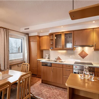 A modern kitchen with wooden furniture and a dining table. The rooms are designed to be bright and inviting.