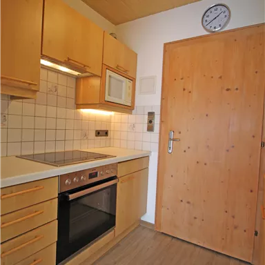 Eine moderne Küche mit Holzschränken und einer Kochstelle. Die Tür ist aus Holz und eine Uhr hängt an der Wand.