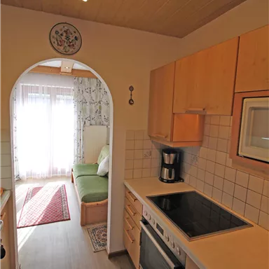 Eine moderne Küche mit Holzschränken und hellen Fliesen. Im Hintergrund ist ein Durchgang zu einem gemütlichen Wohnbereich zu sehen.