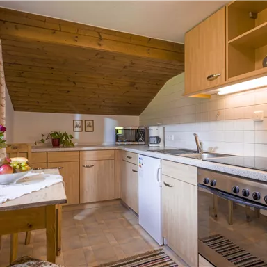 Eine helle Küche mit Holzregalen und modernen Geräten. Auf dem Tisch stehen Blumen und Obst.