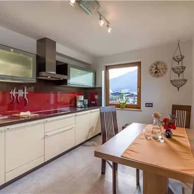 Eine moderne Küche mit rotem Backstein und hellen Möbeln. Ein Esstisch lädt zum Verweilen ein und bietet einen Blick auf die Berge.