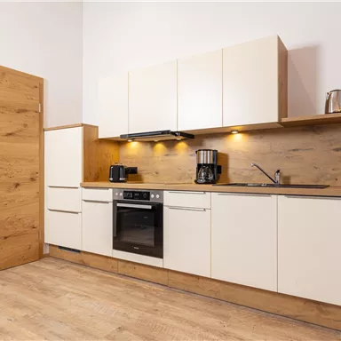 Eine moderne Küche mit hellen Schränken und einem Holzarbeitsblatt. Im Hintergrund sind Küchengeräte und ein Fenster zu sehen.