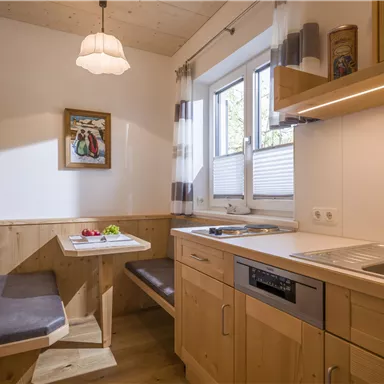 Eine helle Küche mit Holzverkleidung und einem kleinen Essbereich. Es gibt ein Fenster, durch das viel Licht fällt, und eine moderne Kücheneinrichtung.