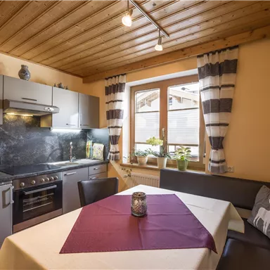 A modern kitchen with a dining table and a cozy seating area. Bright walls and wooden ceilings create an inviting atmosphere.
