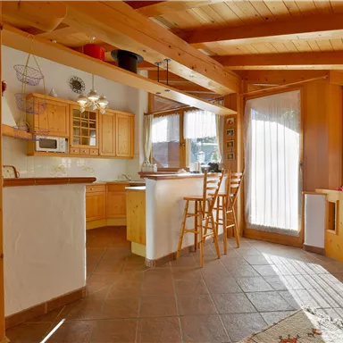 A bright, cozy kitchen with wood paneling and a dining area. Large windows provide plenty of daylight and a welcoming atmosphere.