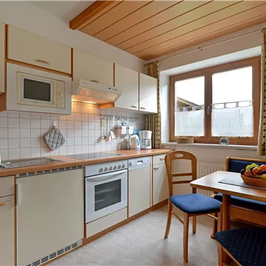 Eine moderne Küche mit hellen Möbeln und Holzdecke. Der Tisch ist mit einer Obstschüssel gedeckt und ein Fenster sorgt für Tageslicht.