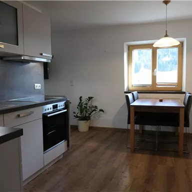 Eine moderne Küche mit einem Esstisch und vier Stühlen. Die Wände sind hell und ein Fenster sorgt für natürliches Licht.